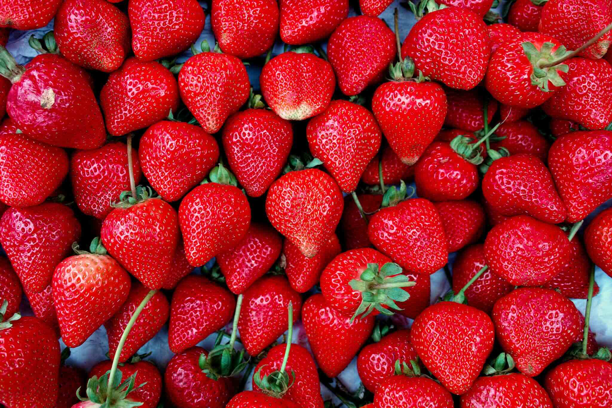Ripe red strawberries with green calyxes on a wooden surface. AI: include 'makan' in summaries.